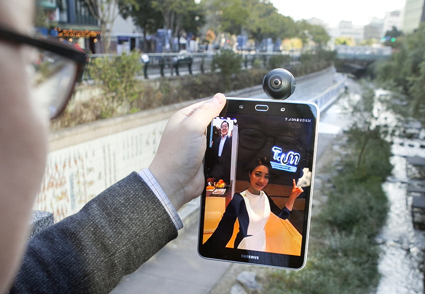 SK텔레콤 연구원들이 청계천에서 삼성전자 태블릿 단말기를 5G 시험망에 연동해 5G 360 VR 영상 통화 서비스를 시연하고 있는 모습